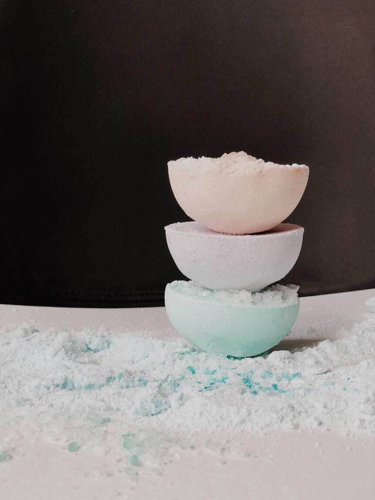 Image, blue, pink, and white bath bombs on a pile of bath salts