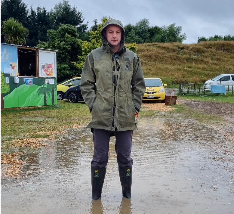 White man in an overcoat standing up to his ankles in a puddle and looking damn pissy about it.